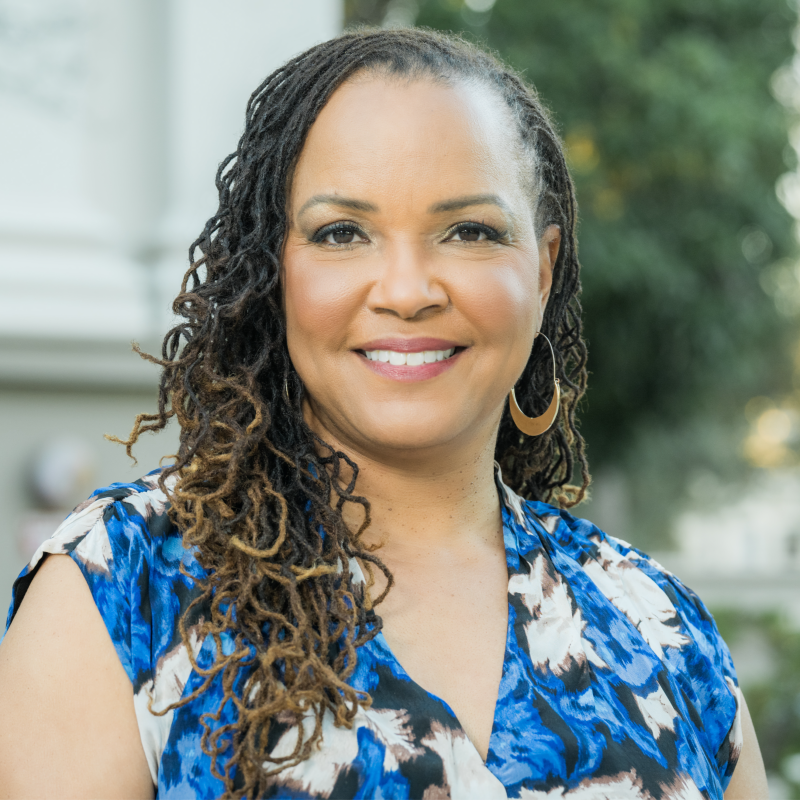 Dr. Niki Elliott smiling outdoors, wearing a blue and white patterned dress